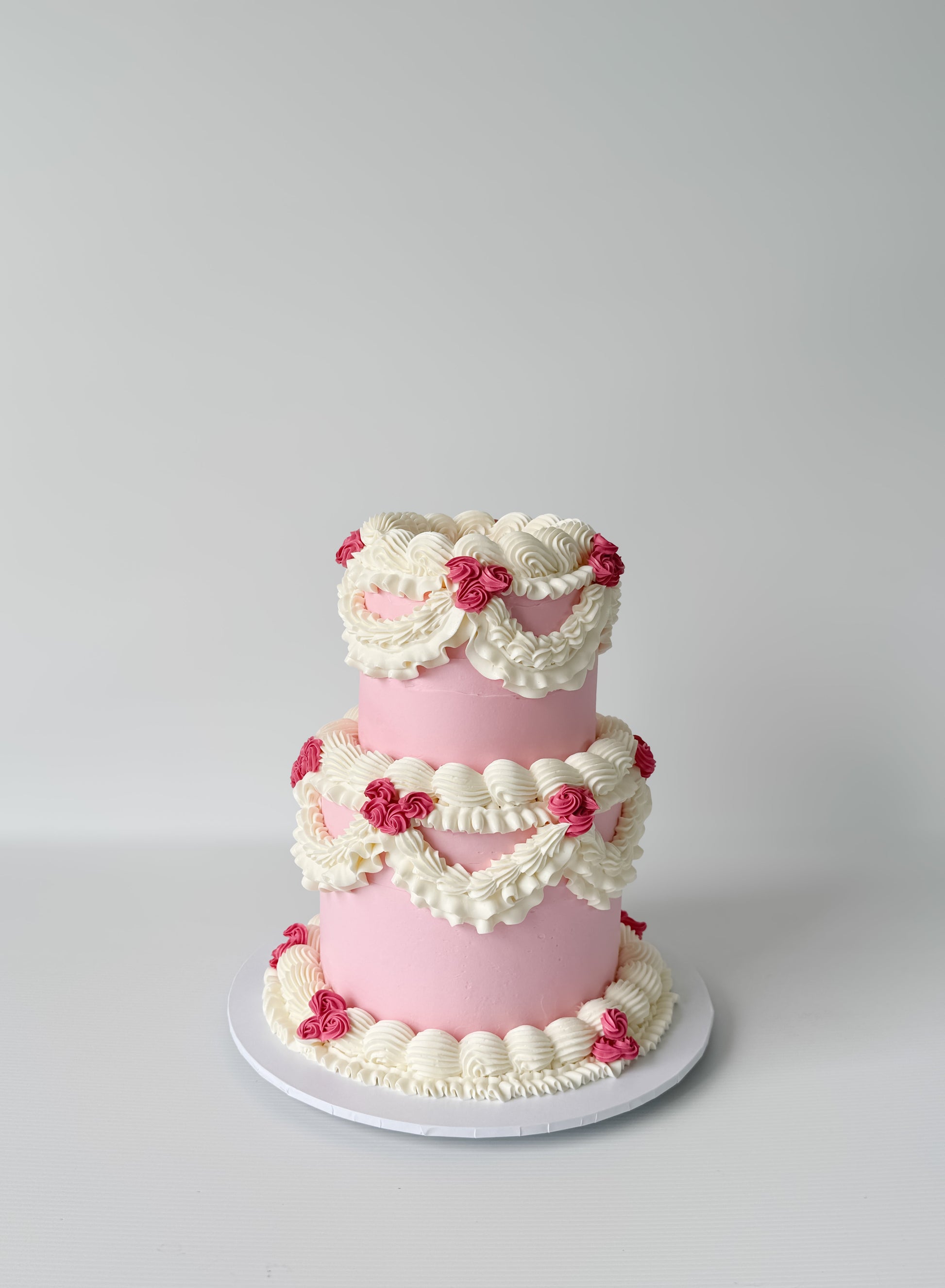 Two-tiered pink cake with white frosting and red flowers on a gray background
