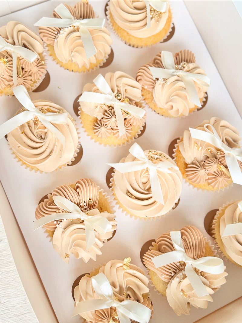 Cupcakes with white frosting and ribbons arranged in a box.