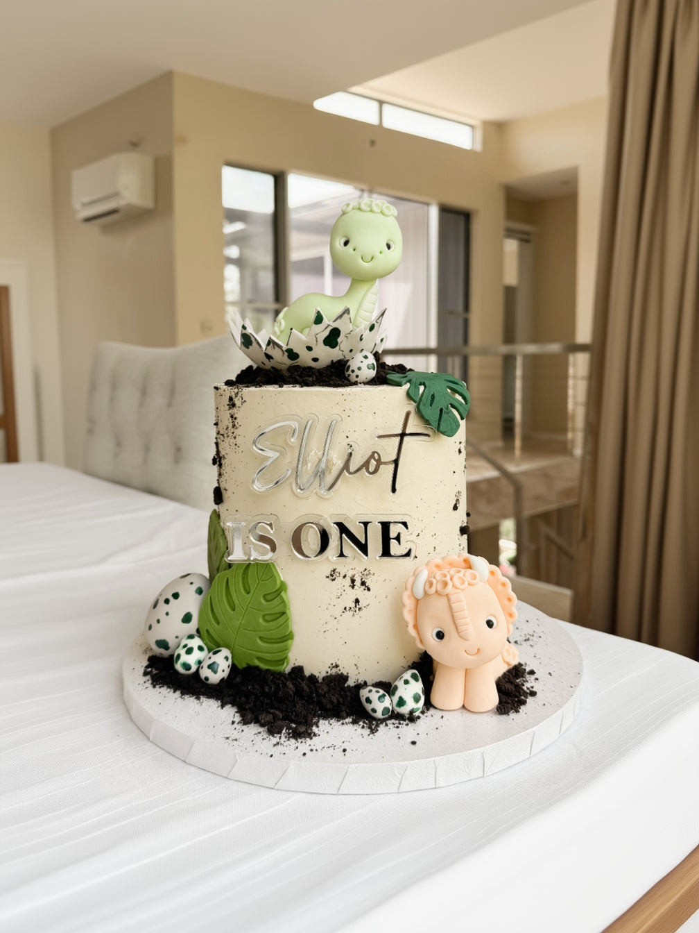 Birthday cake with dinosaur and baby elephant decorations, featuring the text 'Elliot is One'.